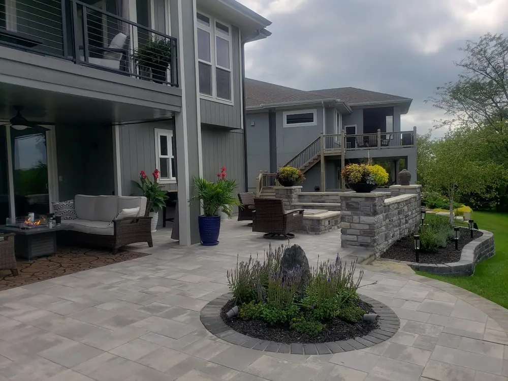 Paver patio with a round planter bed, seat wall and outdoor furniture behind a two-story home