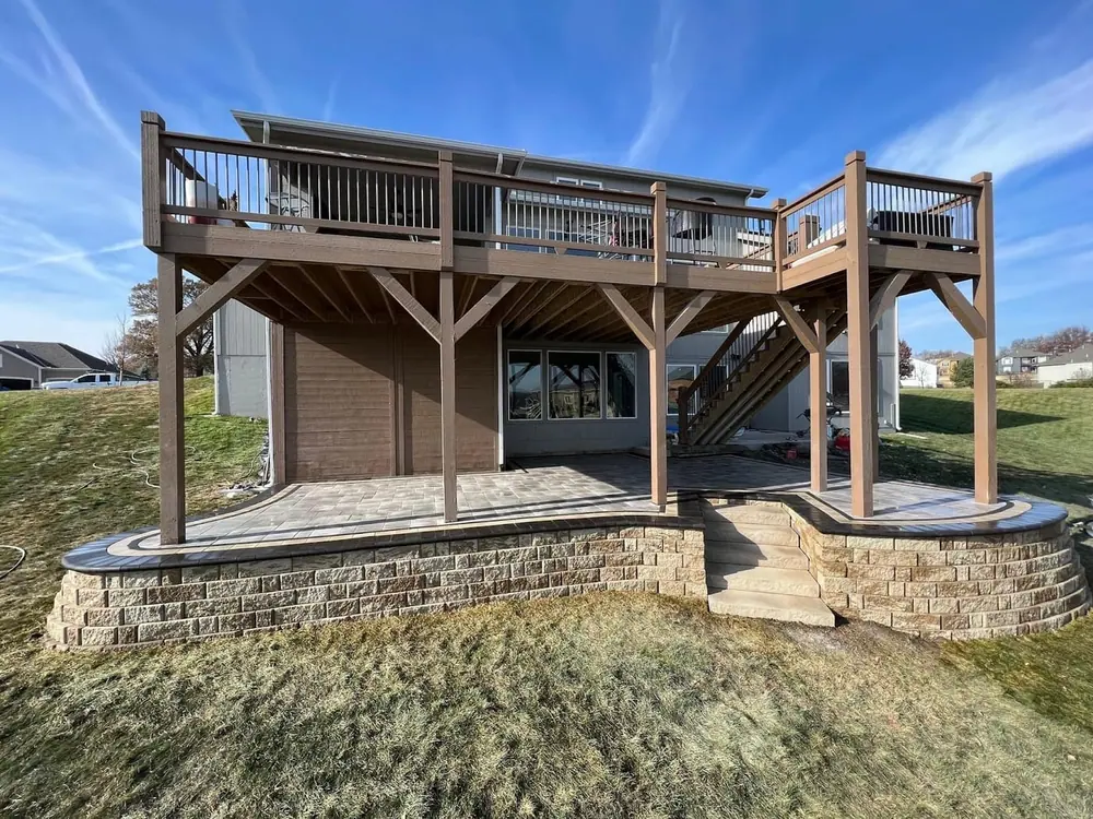 Raised multi-level cedar deck with railings, stairs and a stone base built behind a home