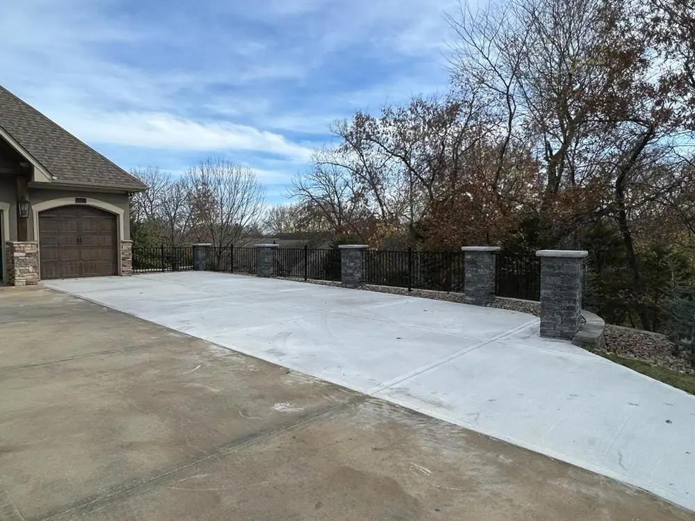 Wide concrete driveway finished between two stone entry pillars