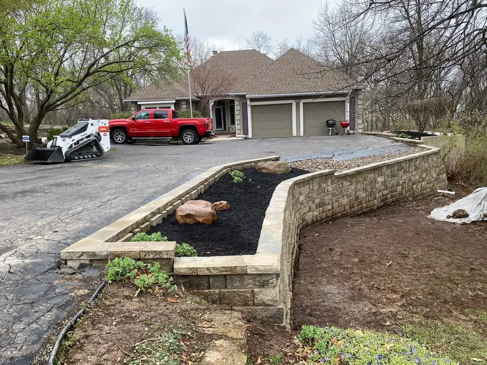 Retaining wall going in along a driveway with fresh mulch beds and a skid steer