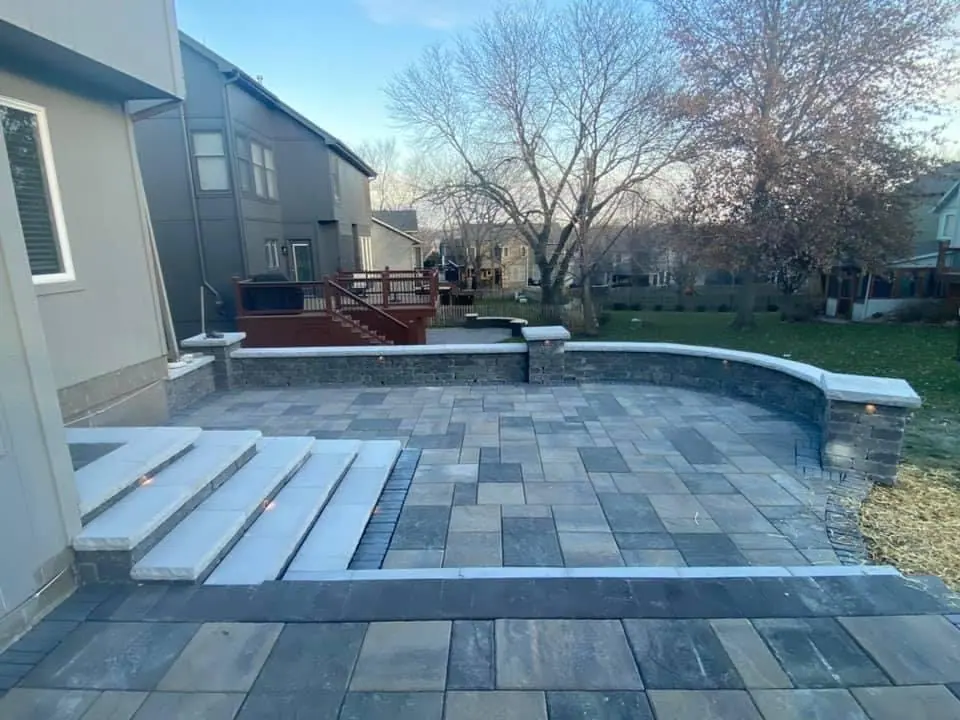 Paver patio with wide steps leading down toward a backyard pool