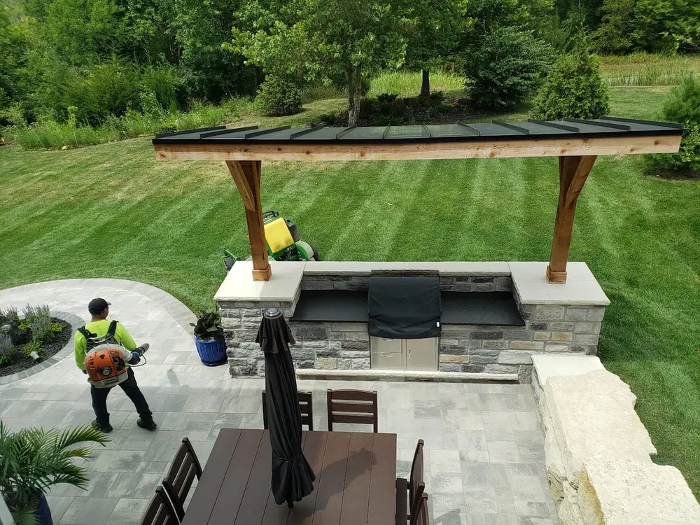Landscaped backyard with a modern pavilion, outdoor kitchen island and a manicured striped lawn