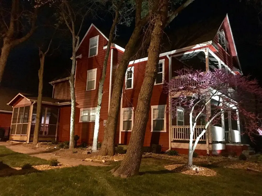 Cabin-style home lit at dusk with landscape uplighting on the trees and deck