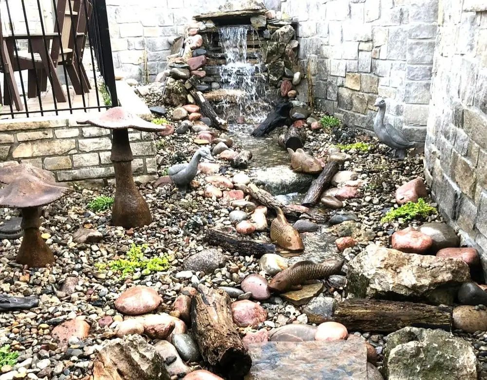 Stacked-stone pondless waterfall built into a wall with river rock at the base