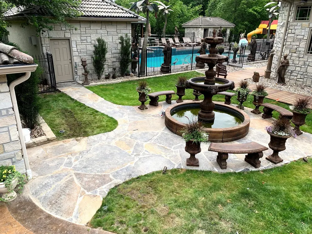 Tiered stone fountain on a flagstone patio surrounded by stone benches and plantings