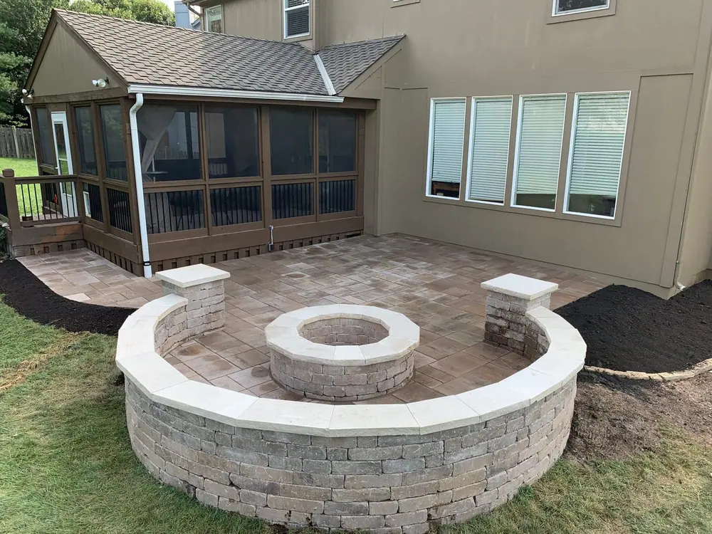 Curved stone seat wall around a fire pit on a paver patio, glowing at dusk