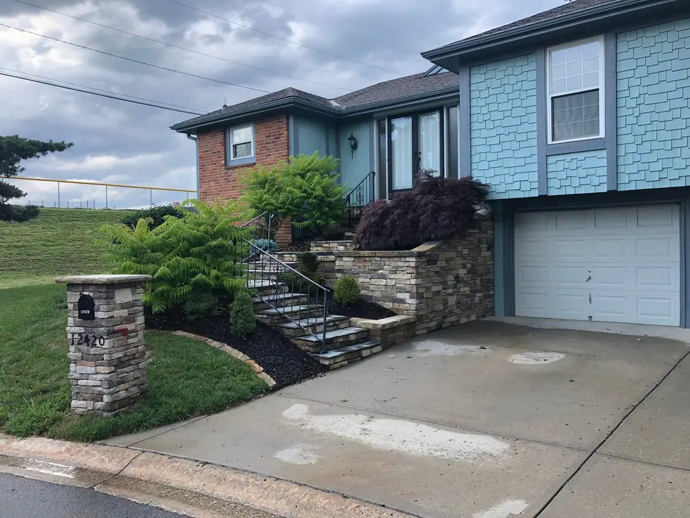 Stone retaining wall with steps and a matching pillar running alongside a driveway